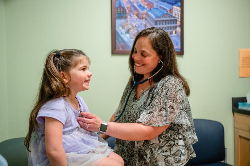 a medical provider using a stethoscope to listen to a young girls heart